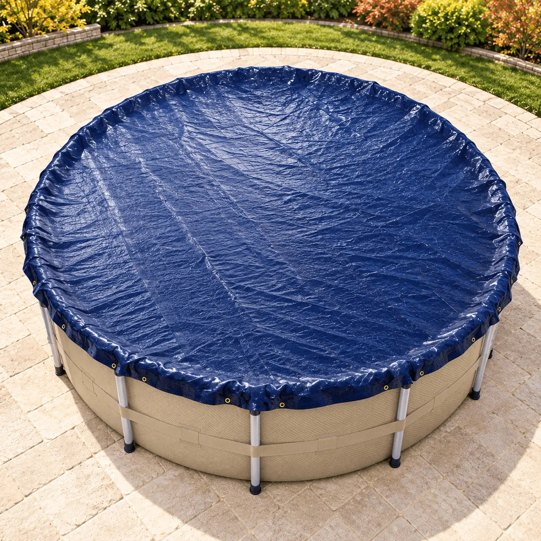 A navy blue pool cover stretched over a beige above-ground swimming pool, photographed from above on a light stone patio with grass and shrubs in the background.