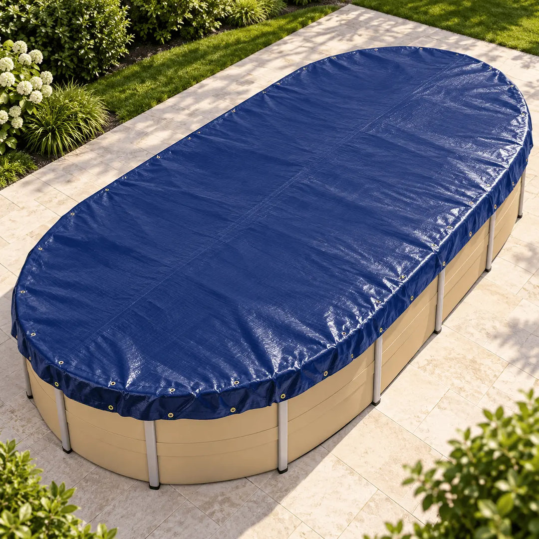 A navy blue oval pool cover secured over a beige above-ground pool, shown from an elevated angle on a light stone patio with green garden plants in the background.