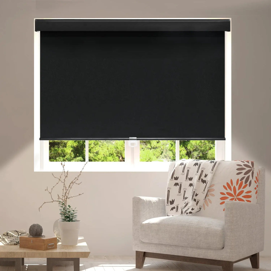 Black blackout roller shade partly lowered over living-room window beside upholstered chair
