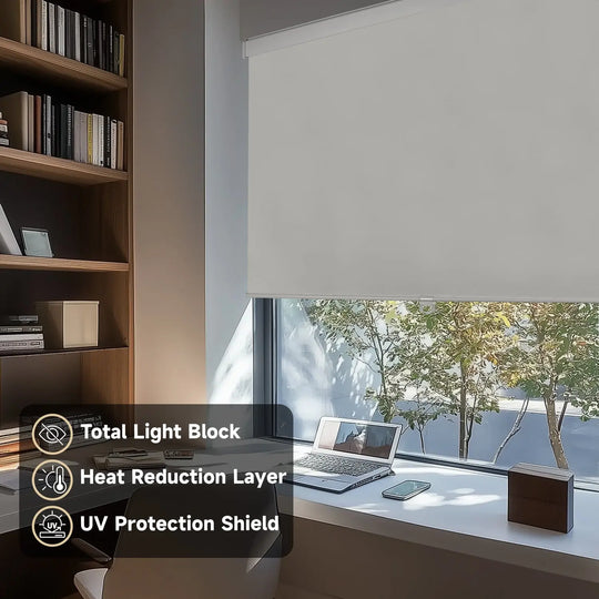 Gray blackout roller shade on home-office window beside laptop and bookcase with light-control labels