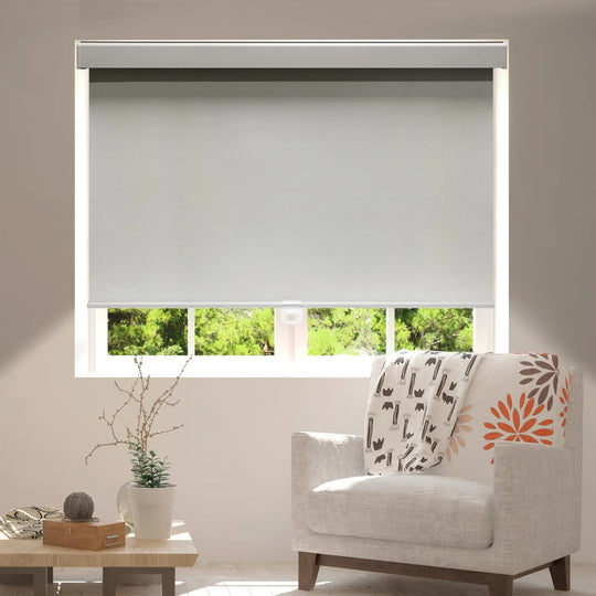 Gray blackout roller shade over living-room window beside upholstered chair